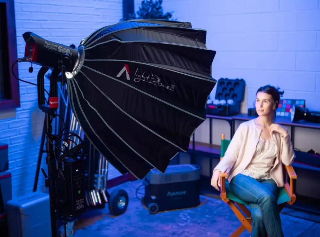 Прожектор Aputure LS 600d Pro із параболічним софтбоксом Light Dome III на стійці освітлює модель у студії із синім фоновим світлом